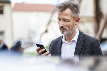 Porträt eines reifen Geschäftsmannes, der auf sein Mobiltelefon schaut - DIGF06031