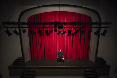 Schauspieler mit Skript auf einer Theaterbühne vor einem roten Vorhang - FBAF00250