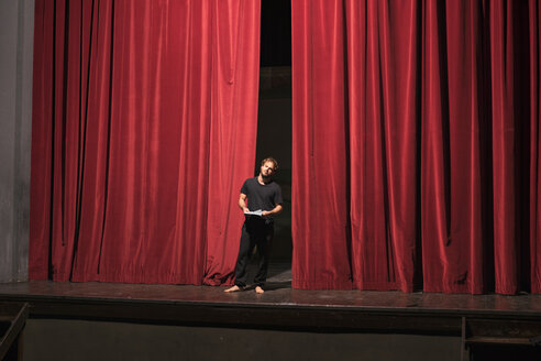 Barefoot actor with script standing on theatre stage - FBAF00261