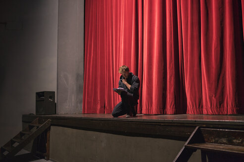 Actor crouching on stage of theatre studying script - FBAF00267