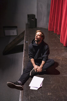 Rehearsing actor sitting on stage of theatre with script - FBAF00271