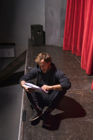 Ein probender Schauspieler sitzt auf der Theaterbühne und betrachtet das Drehbuch, lizenzfreies Stockfoto
