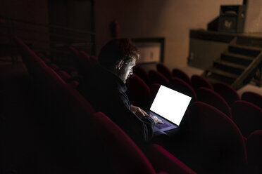 Director sitting at auditorium of theatre working on laptop - FBAF00283