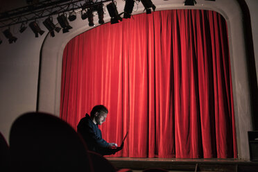 Director standing at auditorium of theatre using laptop - FBAF00286