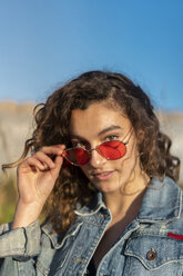 Porträt einer jungen Frau mit lockigem braunem Haar und roter Sonnenbrille - AFVF02576