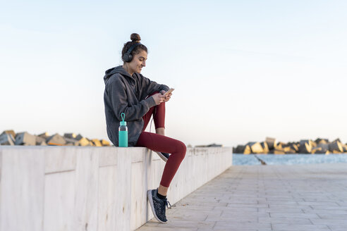Sportive young woman with headphones during workout, using smartphone - AFVF02592