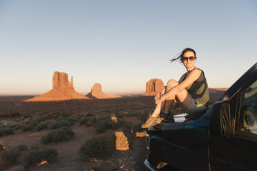 USA, Utah, Monument Valley, Frau sitzt auf der Motorhaube eines Autos und genießt den Sonnenuntergang im Monument Valley - GEMF02866