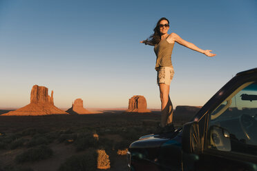 USA, Utah, Monument Valley, Frau steht auf der Motorhaube eines Autos und genießt den Sonnenuntergang im Monument Valley - GEMF02867