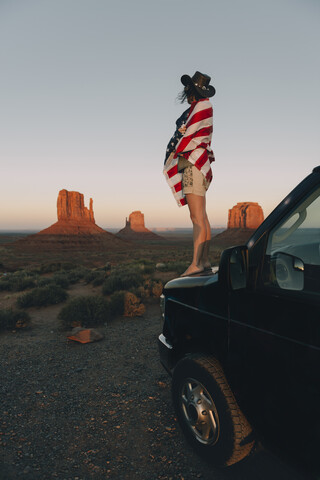 USA, Utah, Monument Valley, Frau mit Flagge der Vereinigten Staaten von Amerika genießt den Sonnenuntergang im Monument Valley, lizenzfreies Stockfoto