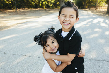 Porträt einer glücklichen Schwester, die ihren Bruder umarmt, während sie auf der Straße im Park steht - CAVF62718