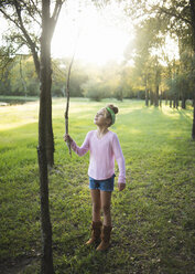 Nettes Mädchen, das einen Stock hält und auf einer Wiese vor Bäumen im Park steht - CAVF62729