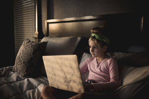 Nettes Mädchen, das einen Laptop benutzt, während es sich zu Hause auf dem Bett entspannt, lizenzfreies Stockfoto