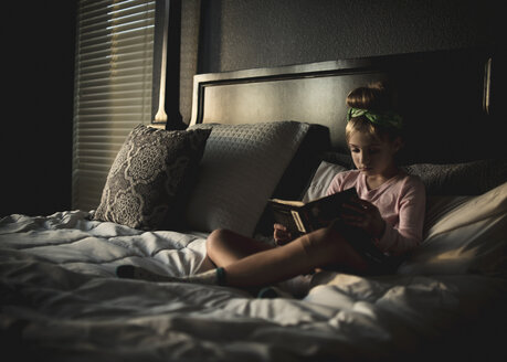 Cute girl reading book while sitting on bed at home - CAVF62732