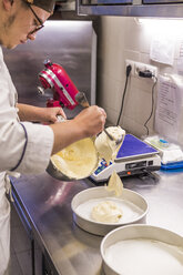 Männlicher Bäcker gießt Teig in Backformen auf dem Küchentisch im Labor - CAVF62745