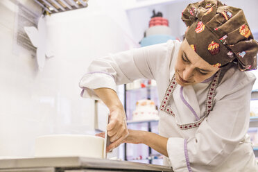 Niedriger Winkel Blick auf weibliche Bäckerin macht Kuchen mit Glätter auf Küchentisch im Labor - CAVF62747