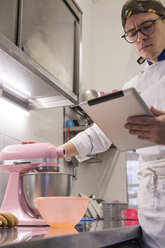 Niedriger Blickwinkel auf einen männlichen Bäcker, der einen Tablet-Computer benutzt, während er einen Mixer auf der Küchentheke im Labor benutzt - CAVF62752