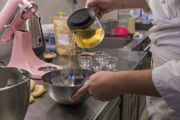 Mittelteil eines männlichen Bäckers, der Wasser in eine Rührschüssel auf dem Küchentisch im Labor gießt - CAVF62756