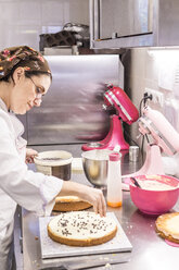 Seitenansicht einer Bäckerin, die einen Kuchen mit Schokoladenstückchen auf einem Küchentisch im Labor dekoriert - CAVF62770