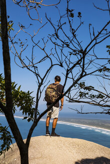 Backpacker in voller Länge mit Blick auf das Meer, während er auf einer Klippe vor blauem Himmel steht - CAVF62779