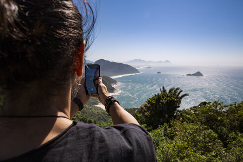 Rückansicht eines Touristen, der das Meer mit seinem Smartphone gegen den Himmel an einem sonnigen Tag fotografiert - CAVF62782