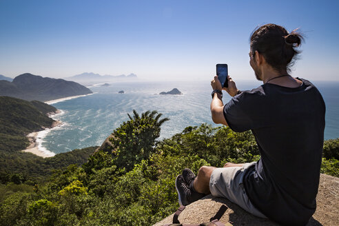 In voller Länge von Touristen fotografieren Meer mit Smartphone, während auf Klippe gegen den Himmel während sonnigen Tag sitzen - CAVF62783