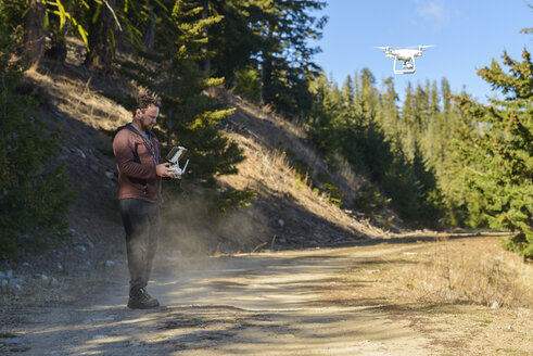 Seitenansicht eines Mannes, der einen Quadcopter fliegt, während er gegen Bäume im Wald steht - CAVF62789