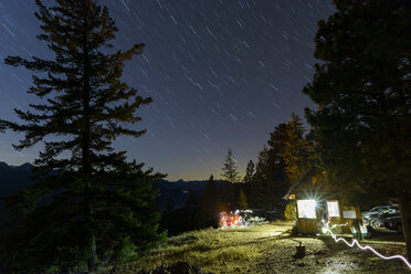 Illuminated cottage amidst trees against star trails in forest at night - CAVF62794