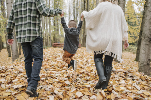 Rückansicht von verspielten Eltern, die ihren Sohn im Herbst im Wald schaukeln und dabei seine Hände halten, lizenzfreies Stockfoto