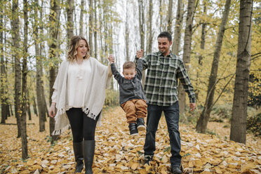 Verspielte Eltern, die ihren Sohn im Herbst im Wald schaukeln und dabei seine Hände halten - CAVF62802