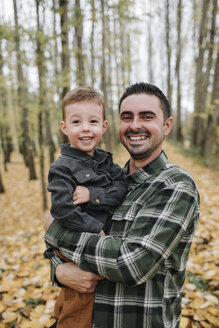 Porträt eines fröhlichen Vaters und eines Sohnes, die im Herbst im Wald stehen - CAVF62806