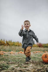 Full length of cute cheerful boy running on pumpkin patch against sky during autumn - CAVF62813