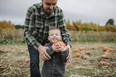 Vater hilft niedlichen lächelnden Sohn beim Halten Kürbis auf Feld im Herbst - CAVF62816