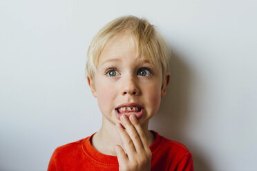 Nahaufnahme eines süßen Jungen, der seine Zähne zeigt, während er zu Hause an der Wand steht - CAVF62831