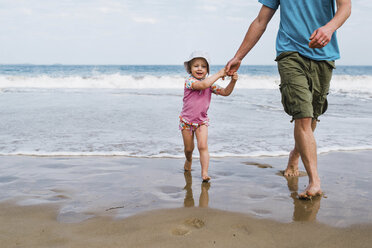 Niedriger Ausschnitt des Vaters, der die Hände seiner süßen Tochter hält, während er am Strand gegen den Himmel läuft - CAVF62833
