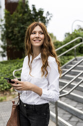 Young businesswoman walking down stairs, using smartphone - GIOF05800
