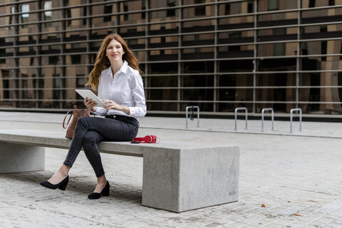 Junge Geschäftsfrau, die auf einer Bank in der Stadt sitzt und ein digitales Tablet benutzt, lizenzfreies Stockfoto