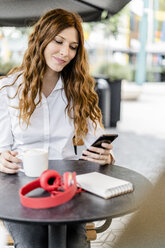 Junge Geschäftsfrau, die in einem Café sitzt und ihr Smartphone benutzt - GIOF05830