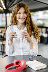 Junge Geschäftsfrau sitzt in einem Café, arbeitet und trinkt Kaffee - GIOF05836
