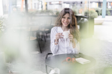 Junge Geschäftsfrau sitzt in einem Café, arbeitet und trinkt Kaffee - GIOF05837