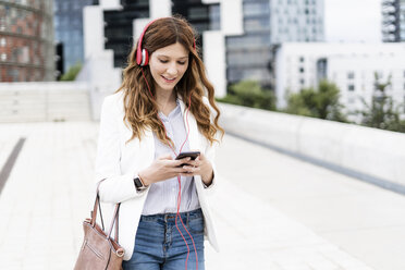 Young businesswoman commuting in the city, using smartphone and headphones - GIOF05849