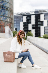 Junge Geschäftsfrau beim Pendeln in der Stadt, mit Smartphone und Kopfhörern - GIOF05850
