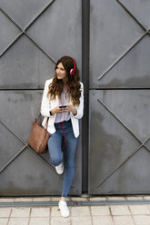 Young businesswoman commuting in the city, using smartphone and headphones - GIOF05851