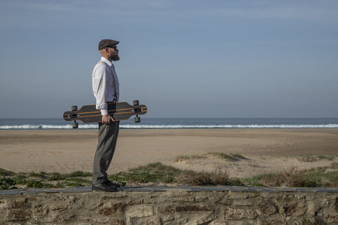 Mann mit Longboard steht auf einer Mauer vor Strand und Meer - KBF00575