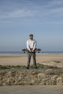Mann mit Longboard steht auf einer Mauer vor Strand und Meer - KBF00576
