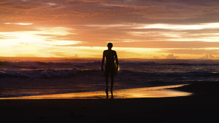 Full length of silhouette tourist with surfboard looking at sea while standing on shore against sky during sunset - CAVF62888