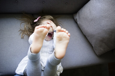 Hohe Winkel Ansicht der glücklichen Mädchen versteckt Gesicht, während auf dem Sofa zu Hause liegen, lizenzfreies Stockfoto