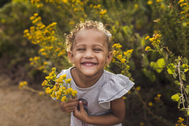 High angle portrait of happy girl with holding flowers while standing plants in park - CAVF62903