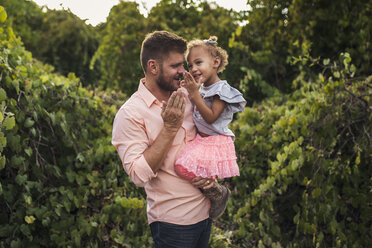 Father carrying cute daughter while standing against plants in park - CAVF62904