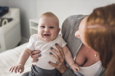 High angle view of mother holding cute son while sitting on bed at home - CAVF62909