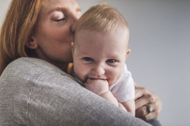 Nahaufnahme einer Mutter, die ihren süßen Sohn küsst, während sie ihn gegen eine graue Wand zu Hause trägt - CAVF62913